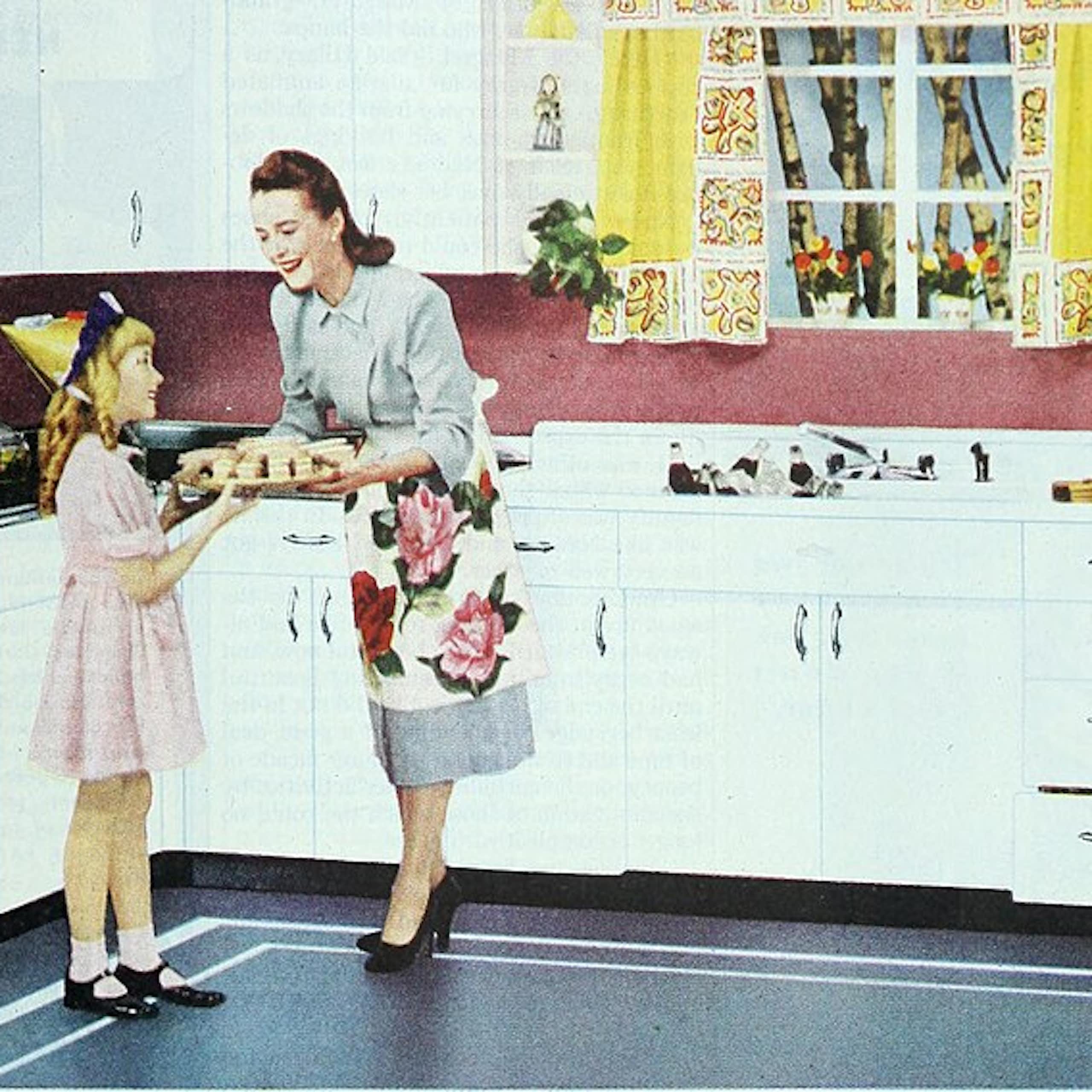 A view of a kitchen with a man on one side wearing a tie, smoking a pipe and reading a newspaper, while near the stove, a woman in a dress and an apron hands a plate of food to a child.