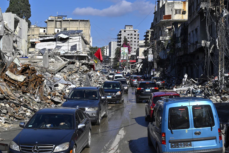 A line of traffic makes its way through a war-damaged city.