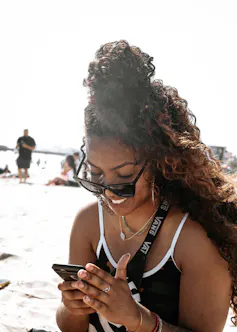 A young woman sitting outdoors smiles as she looks at her phone.