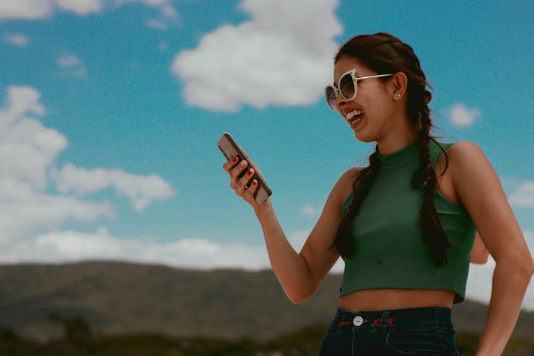 A young woman smiles looking at her phone outdoors.