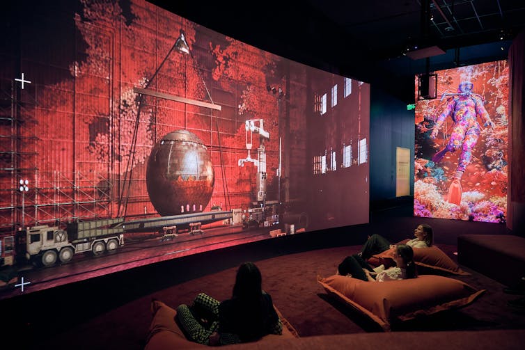 People sit on beanbags in front of red screens.
