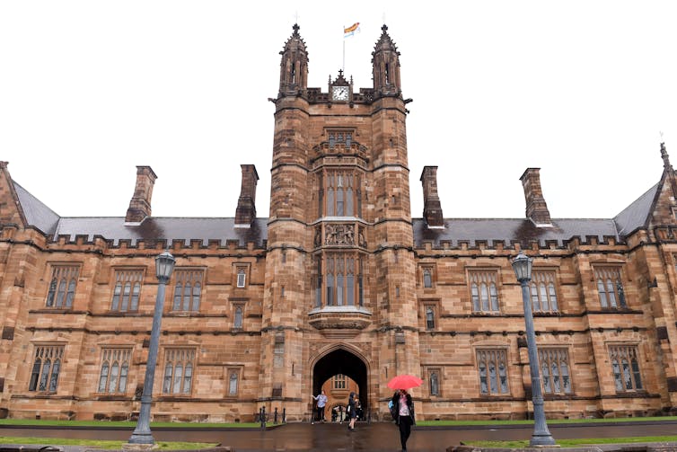 The main sandstone building of Sydney University. People walk with umbrellas.