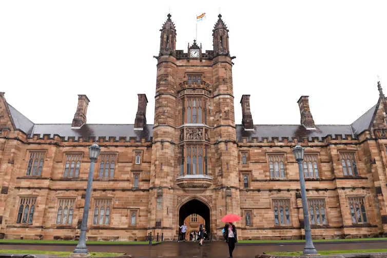 The main sandstone building of Sydney University. People walk with umbrellas.