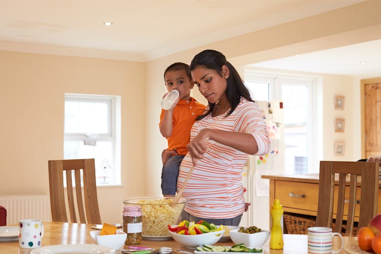 A pregnant mother holding a toddler while preparing food in kitchen