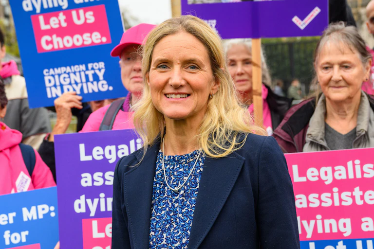 Kim Leadbeater in front of a group of campaigners holding blue and pink signs in support of legalising assisted dying