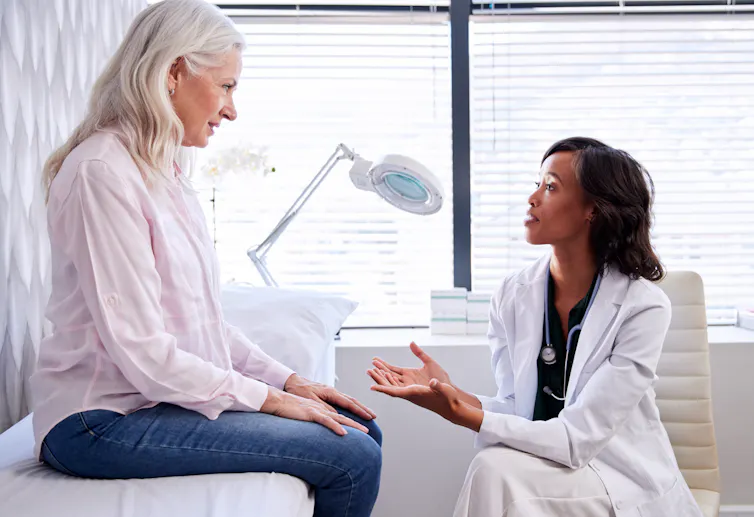 A woman sitting on an examination table talking to a doctor