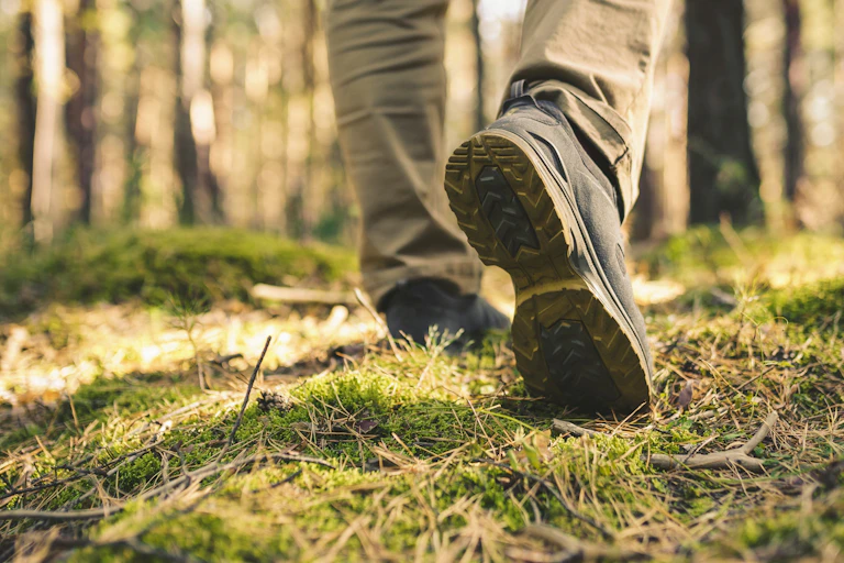 feet of person in walking boots walking on grass, forest trees in background