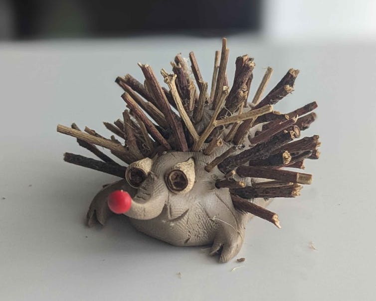 Closeup of a clay model echidna with sticks for spikes and gumnuts for eyes, resting on a light coloured table