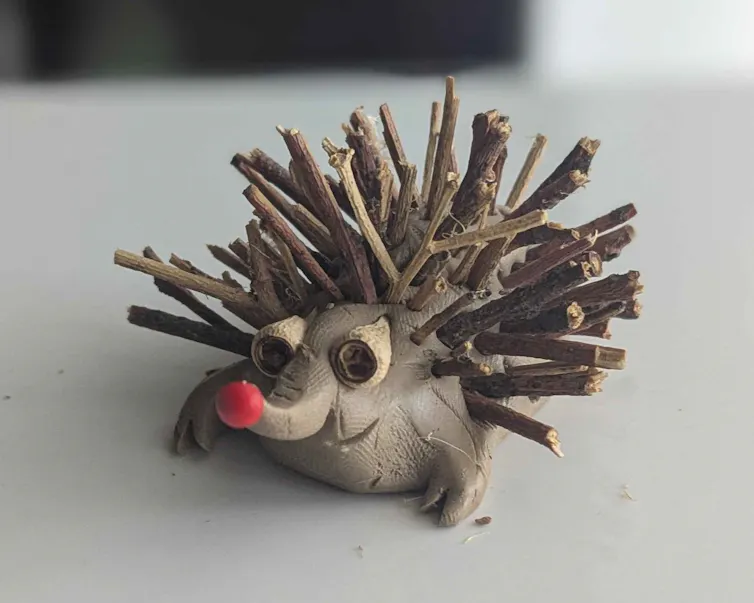 Closeup of a clay model echidna with sticks for spikes and gumnuts for eyes, resting on a light coloured table