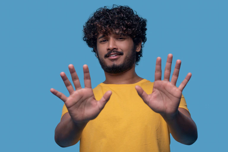 A young man holds up both hands to the camera.