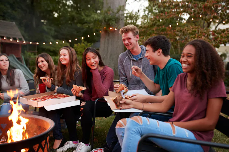 A group of teenagers enjoying a pizza in a garden.