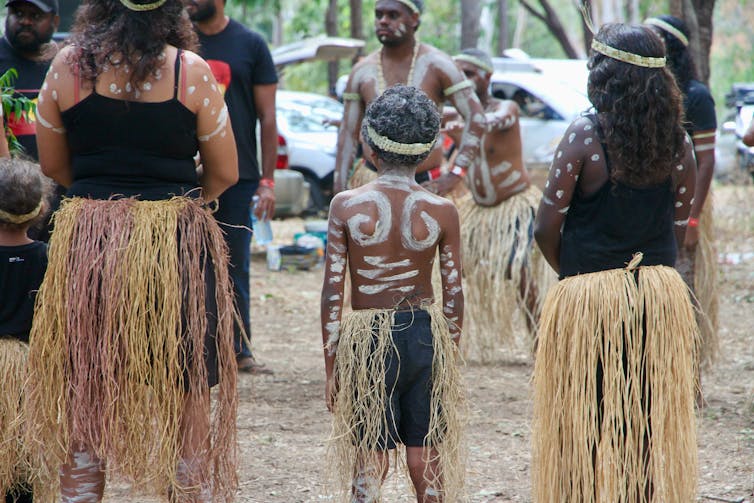 The backs of an Indigenous woman and two children in traditional dress.