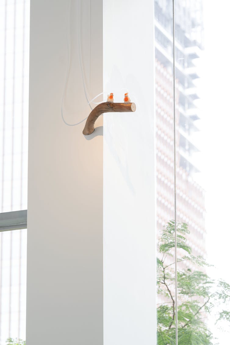 Two ceramic birds on a wooden branch, near a window.