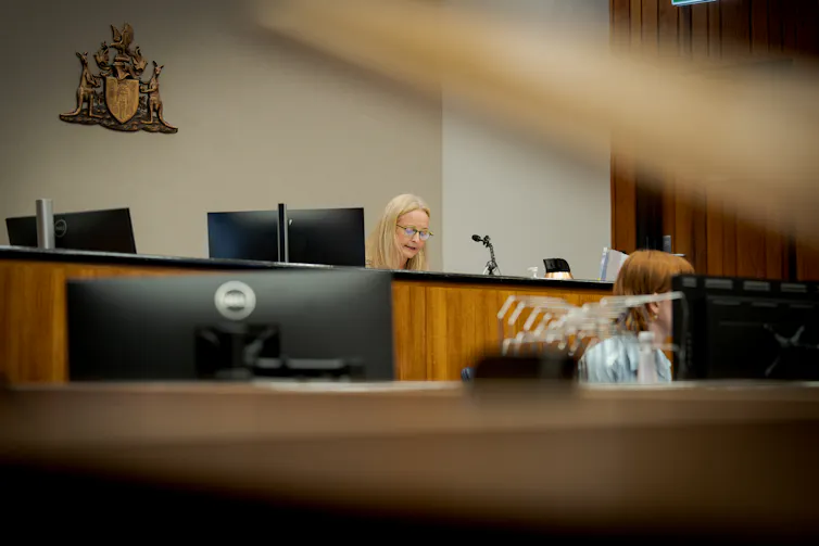 A woman behind a wooden desk speaks into a microphone