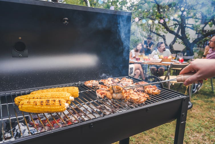 corn and chicken on barbecue grill with partygoers in background