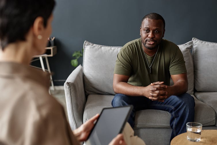 A man in a dark green t-shirt receiving counselling from a female professional.