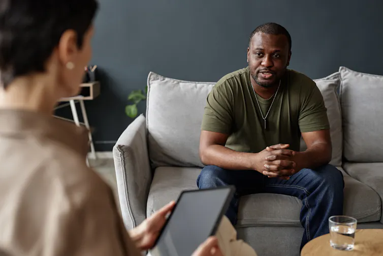 A man in a dark green t-shirt receiving counselling from a female professional.