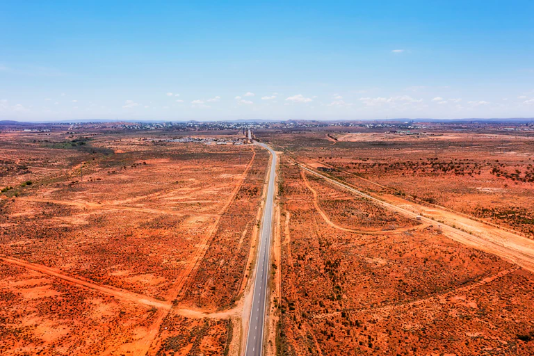 Empty road through a red desert leading to a town in the distance.