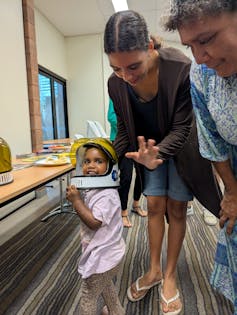 A young Aboriginal girl wearing an astronaut helmet and smiling.