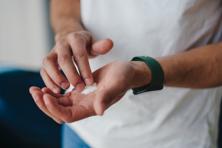 A man's finger touches moisturiser cream in his palm.