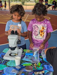 Two young Aboriginal children look down a microscope.