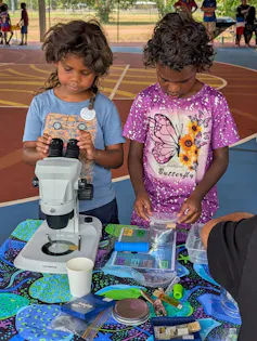 Two young Aboriginal children look down a microscope.
