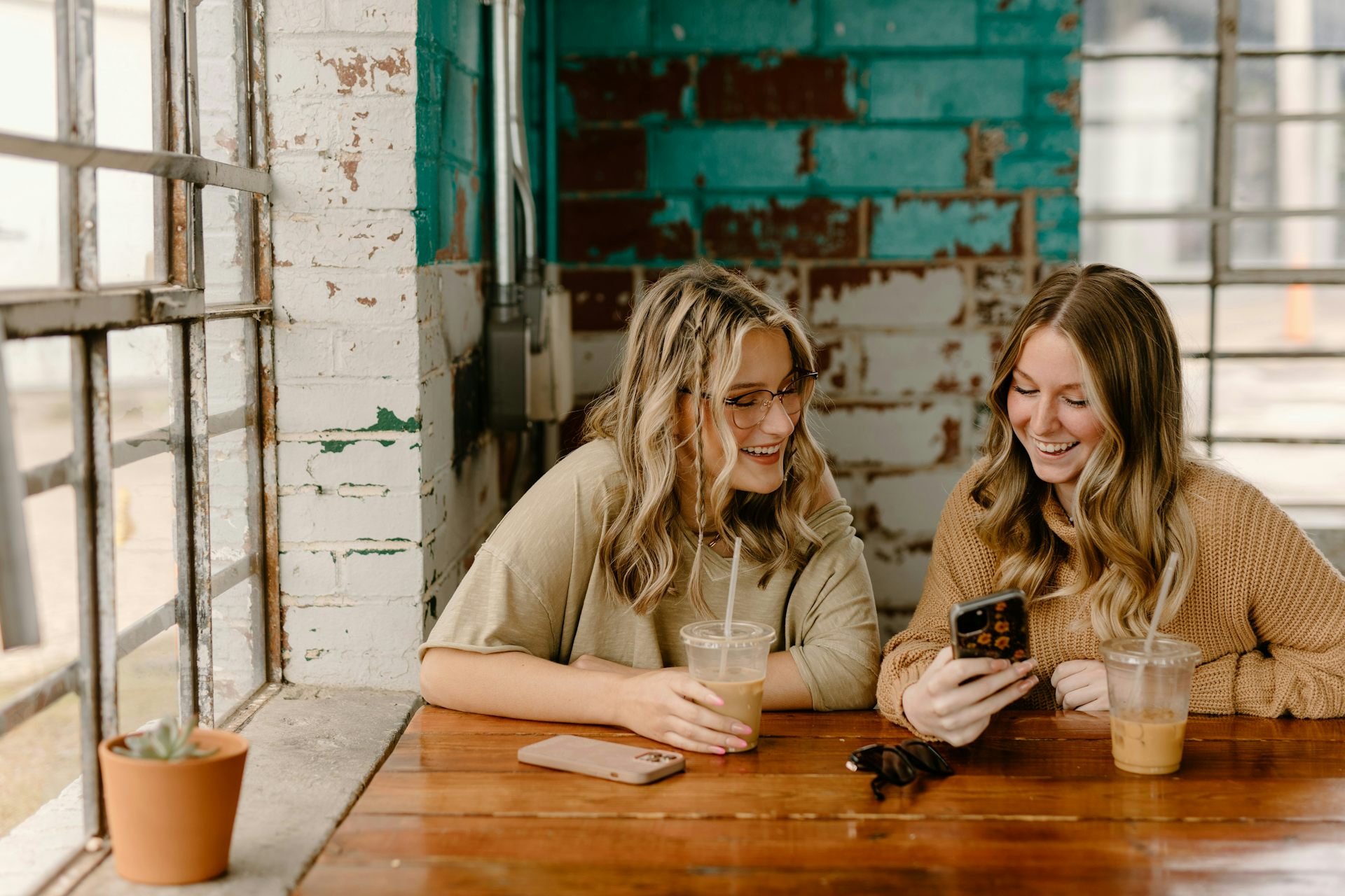 Two blonde women smile looking at a phone.