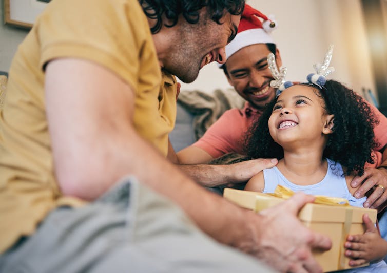 Two dads and their daughter exchanging gifts.