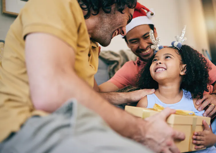 Two dads and their daughter exchanging gifts.