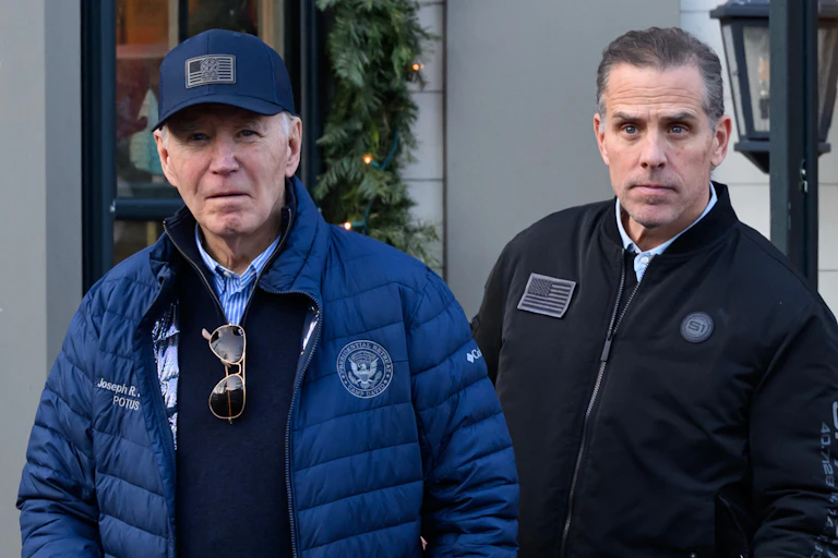 Two men in bomber jackets stand outside a building.