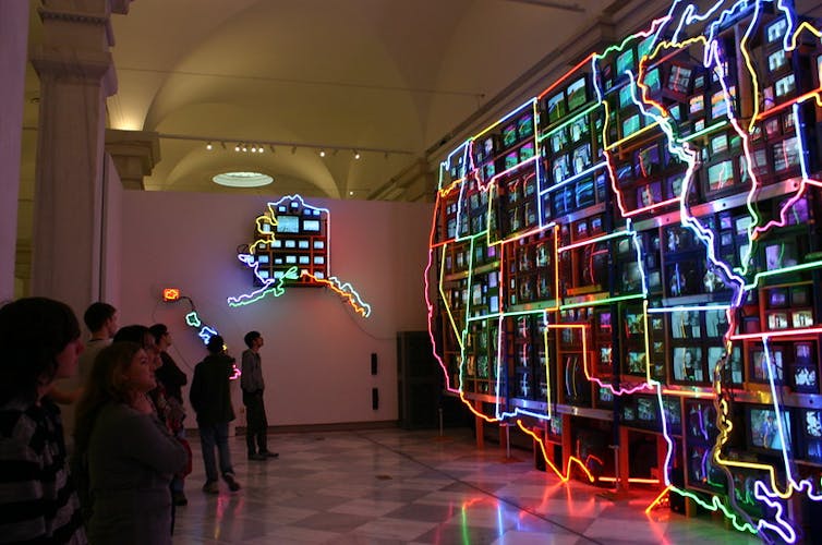 Neon lights outline shapes of the U.S. states with many videos playing inside the shapes