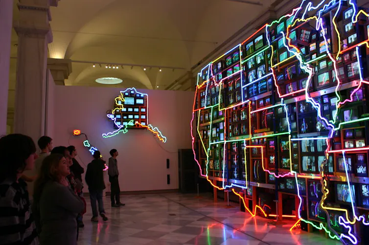 Neon lights outline shapes of the U.S. states with many videos playing inside the shapes