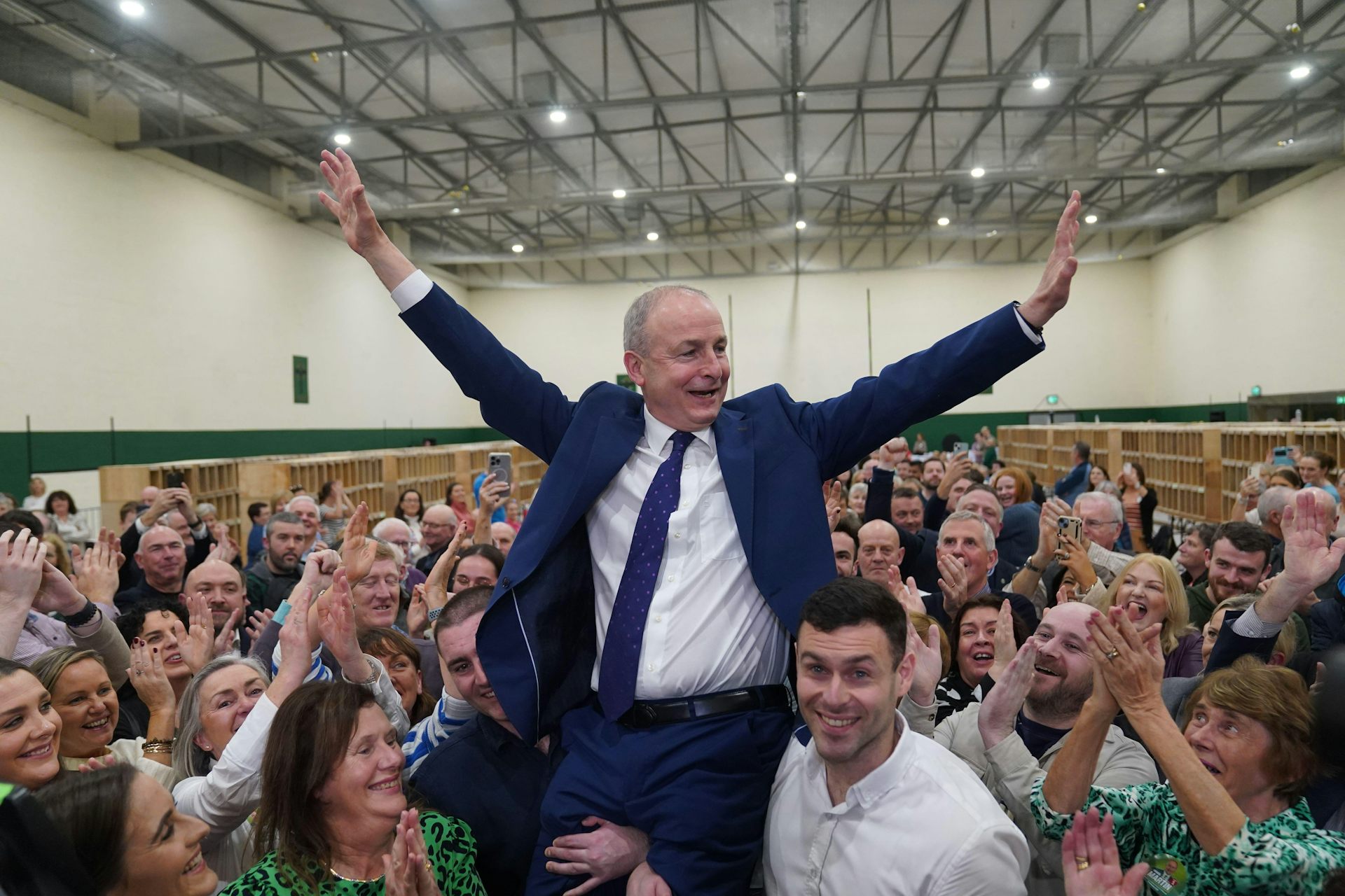 In an election count centre, Martin is hoisted into the air by his sons, celebrating with his hands in the air