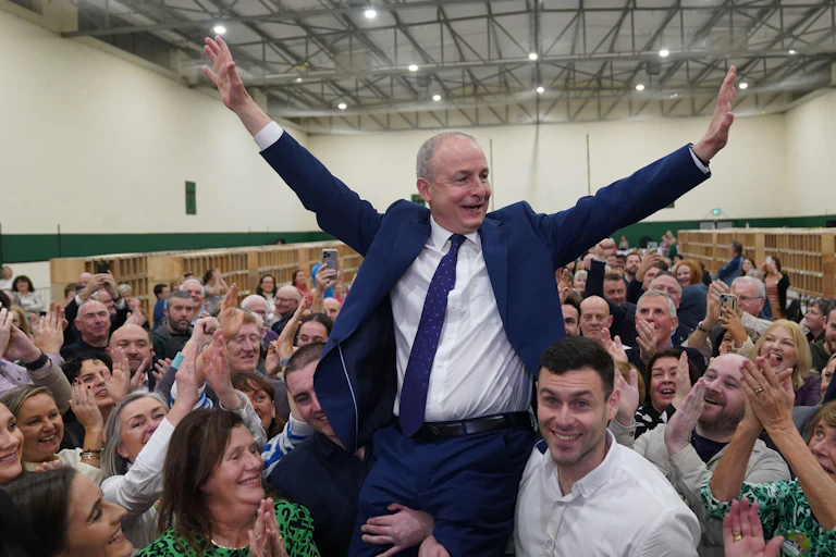 In an election count centre, Martin is hoisted into the air by his sons, celebrating with his hands in the air