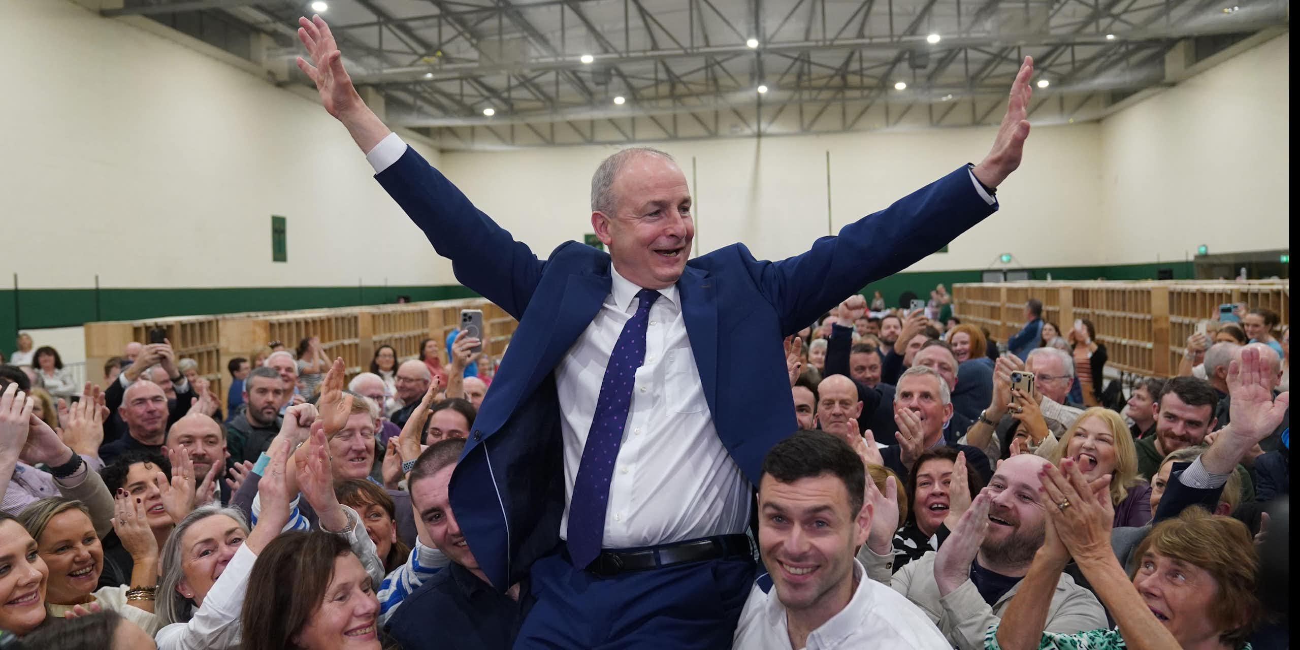 In an election count centre, Martin is hoisted into the air by his sons, celebrating with his hands in the air