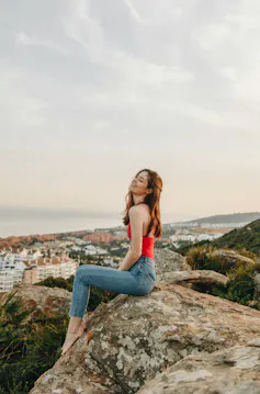 Una mujer de pelo largo, blanca, delgada y alta, sentada en una roca.