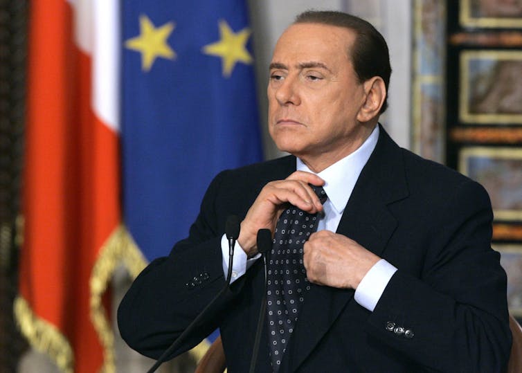 A man with slicked-back black hair adjusts his tie.