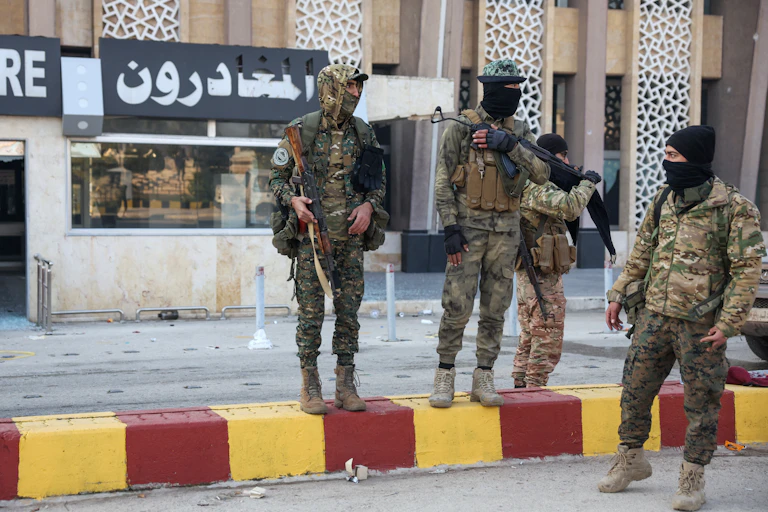 A group of men in army fatigues stand around holding guns.