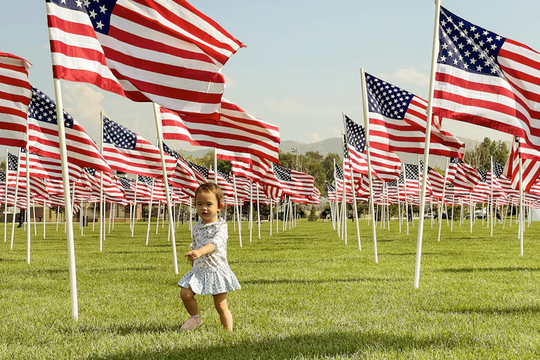 A young child runs in a field with rows and rows of American flags on posts across the grass.