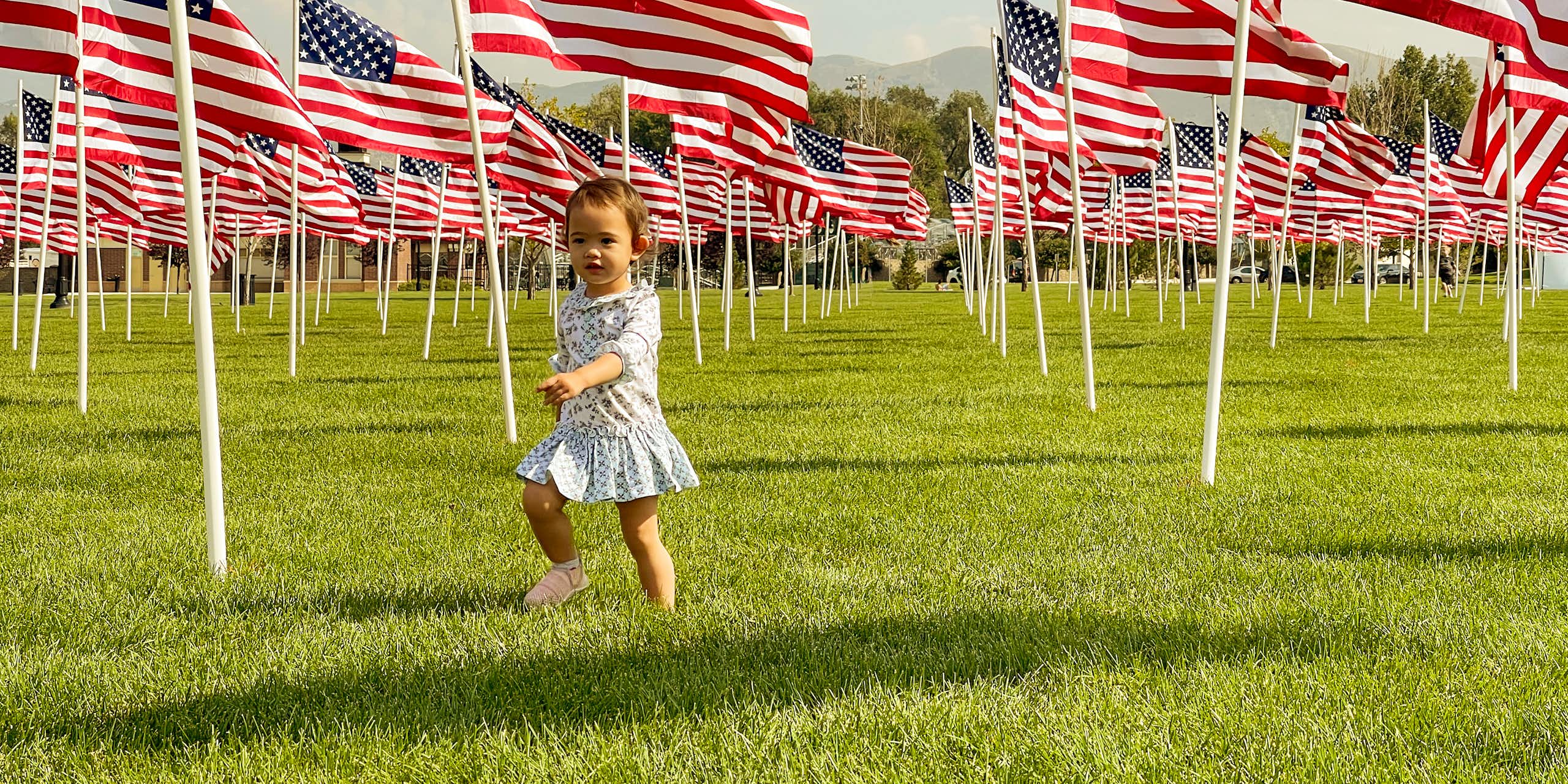 A young child runs in a field with rows and rows of American flags on posts across the grass.