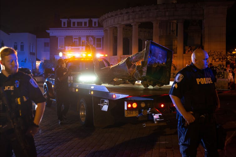 The Jefferson Davis statue is loaded onto a tow truck at night, police look on.