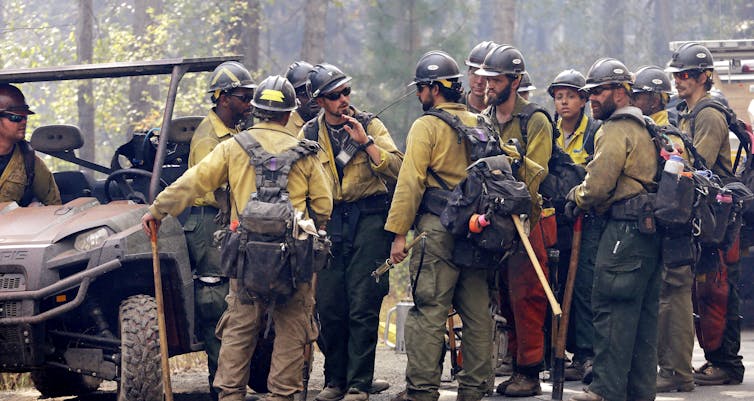 A group of firefighters with their geat ready to head toward a fire stands around a crew leader.
