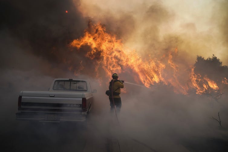 A firefighter holds a fire hose shooting water at a wall of flames burning along a road near Irvine, California, in 2020.