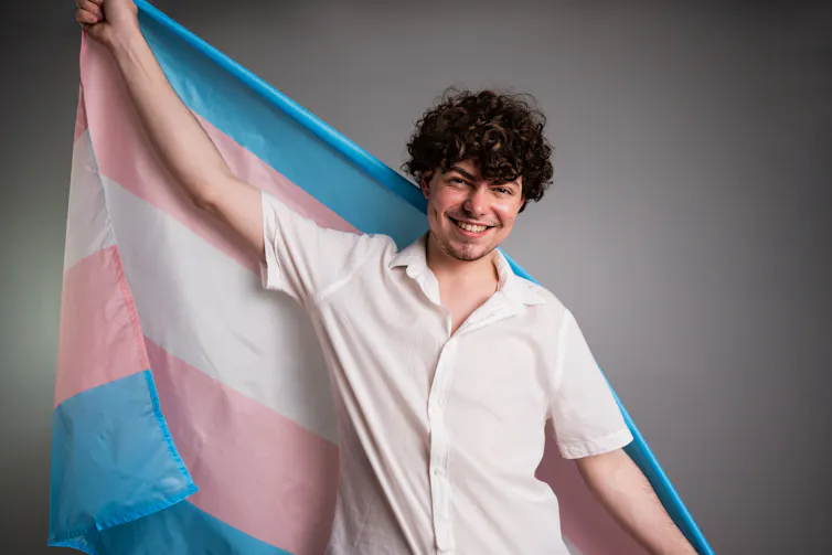 A young transgender man holding transgender flag.