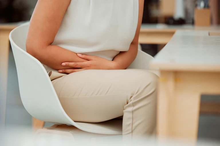 A person, seen from the neck down, clutches their arms across their lower stomach while sitting