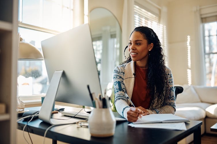 A woman speaks into a headset while working on a computer