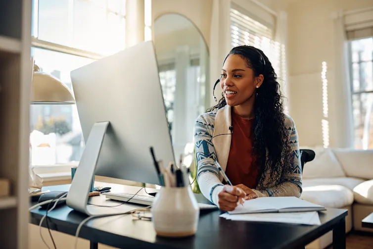 A woman speaks into a headset while working on a computer