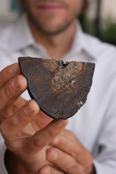 A hand holding a semi-circular rock with a metallic sheen