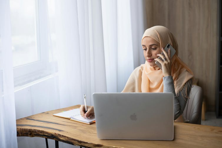 Muslim woman talking on the phone and taking notes.