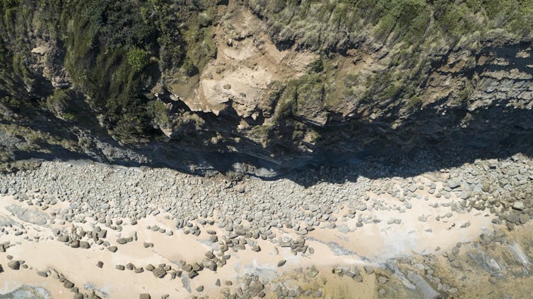 Aerial view of a jagged cliff with many smaller fallen rocks underneath it.